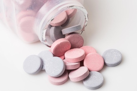 Heartburn pill bottle spilling blue and pink antacid pills on white background; Concept of “Can I take Pepcid or Prilosec Indefinitely?”